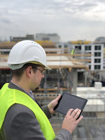 Arbeiter mit Helm steht auf Baustelle und nutzt COMAN Software zum Dokumentieren des Bauprojekts